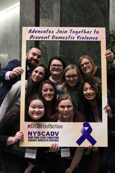 Advocates Join Together To Prevent Domestic Violence (group poses within a frame board sign)